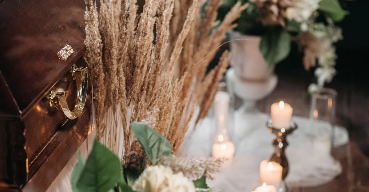 Un arrangement funéraire élégant avec un cercueil en bois, des fleurs et une bougie à l'intérieur.