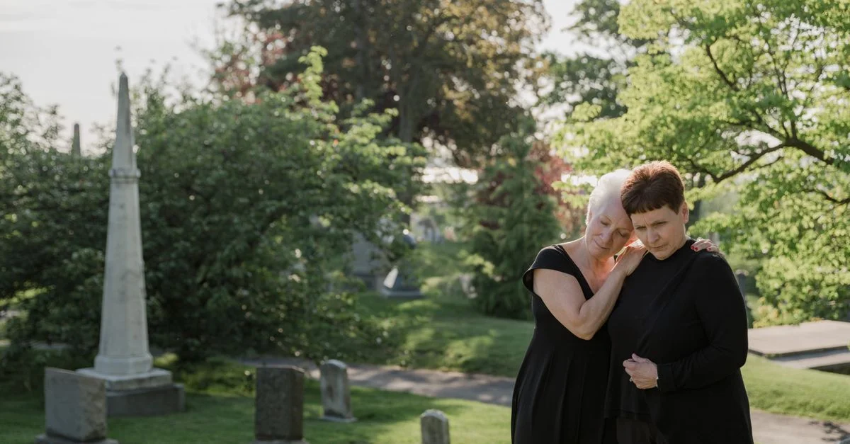 Deux femmes en vêtements noirs font leur deuil dans un cimetière paisible.