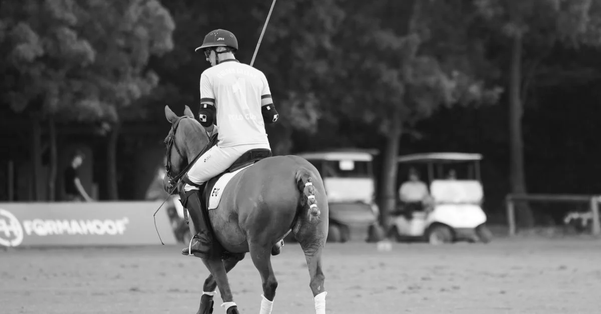 Image noir et blanc d'un joueur de polo à cheval pendant un match, soulignant l'élégance et le sport.