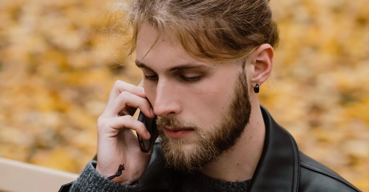 Gros plan sur un homme barbu avec une boucle d'oreille passant un appel téléphonique lors d'une belle journée d'automne.