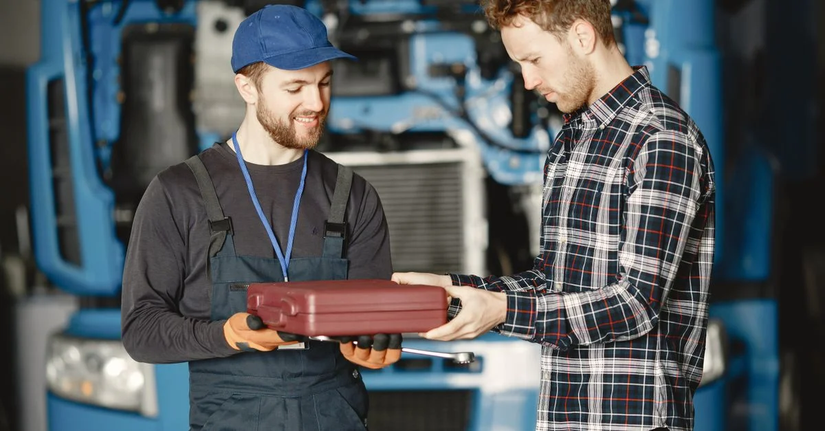 Deux mécaniciens discutant du travail dans un atelier de garage, tenant une boîte à outils.