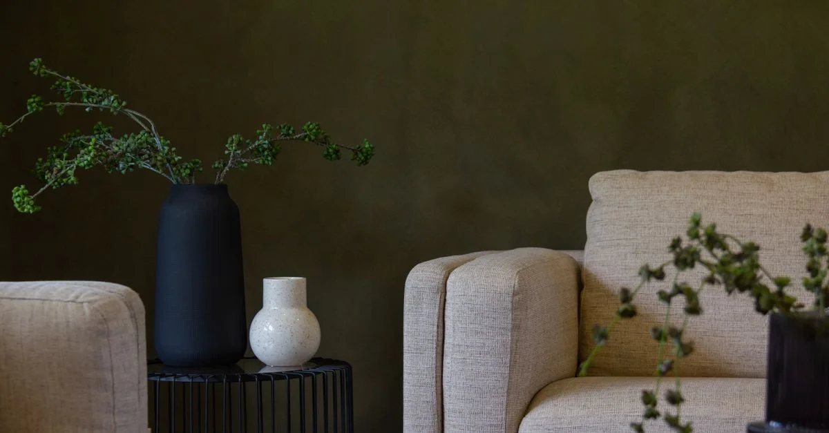 Un salon élégant et minimaliste avec des meubles modernes et une décoration, présentant des murs verts et des tons neutres.