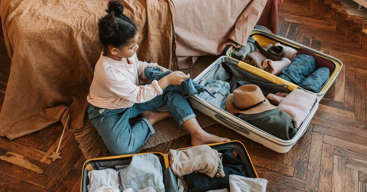 Jeune enfant assise sur un lit en train de préparer une valise pour des vacances familiales à venir.